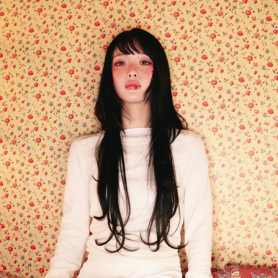 HANRORO in a white outfit against yellow floral wallpaper