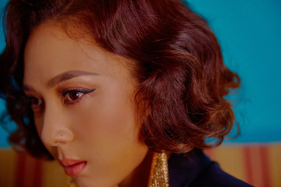 Yoon Mirae with short auburn waves and gold earrings against a teal background, in a Gemini 2 promotional portrait
